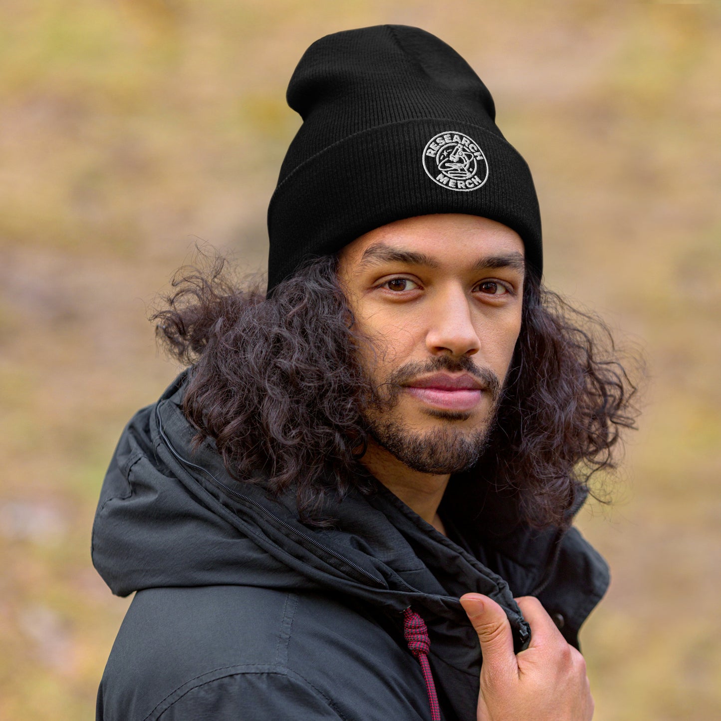 Schwarze gestrickte Beanie mit Research Merch Logo, getragen von einer Person im Outdoor-Setting mit unscharfem Hintergrund.