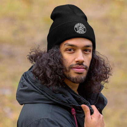Schwarze gestrickte Beanie mit Research Merch Logo, getragen von einer Person im Outdoor-Setting mit unscharfem Hintergrund.